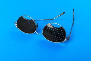 Two different type of glasses on blue background. Medical concept. Top view. Pinhole black eyeglasses help relaxing weary eyes Isolated on white background. Classic Fashion optical eyeglasses photo