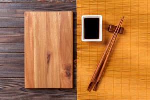Empty rectangular wooden plate with chopsticks for sushi and soy sauce on wood background. Top view with copy space photo