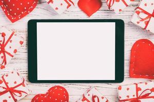 pantalla en blanco de tableta digital con caja de regalo y decoración de corazones en mesa de madera. vista superior. fondo del concepto del día de san valentín foto