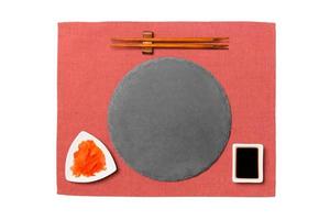 Emptyround black slate plate with chopsticks for sushi, ginger and soy sauce on red napkin background. Top view with copy space for you design photo