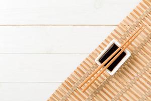 Bamboo mat and soy sauce with sushi chopsticks on white wooden table. Top view with copy space background for sushi. Flat lay photo