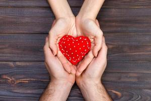 Red heart in woman and man hands,on wooden background photo