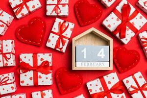 vista superior del calendario de madera, cajas de regalo blancas y corazones textiles rojos sobre fondo colorido. concepto del día de san valentín foto