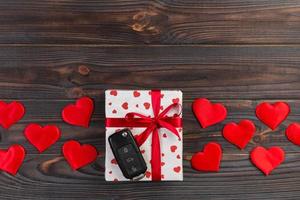 Valentine or other holiday handmade present in paper with red hearts, car keys and gifts box in holiday wrapper. box gift on Dark wooden table top view with copy space, empty space for design photo