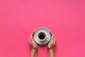 Minimalistic style woman hand holding a cup of coffee on pink background. Flat lay, top view photo