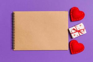 Top view of craft notebook surrounded with gift box and hearts on colorful background. Valentine's Day concept photo