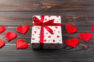 Valentine or other holiday handmade present in paper with red hearts and gifts box in holiday wrapper. Present box of gift on Dark wooden table top view with copy space, empty space for design photo