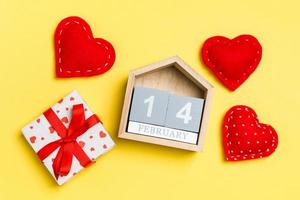composición de calendario de madera, cajas de regalo blancas de vacaciones y corazones textiles rojos sobre fondo colorido. catorce de febrero. concepto del día de san valentín foto