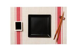 Empty black square plate with chopsticks for sushi and soy sauce on sushi mat background. Top view with copy space for you design photo