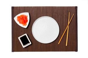 Empty round white plate with chopsticks for sushi, ginger and soy sauce on dark bamboo mat background. Top view with copy space for you design photo