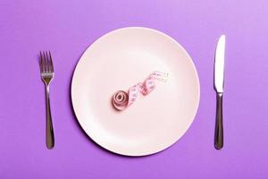 concepto de dieta saludable de plato con cinta métrica, tenedor y cuchillo sobre fondo morado. vista superior foto