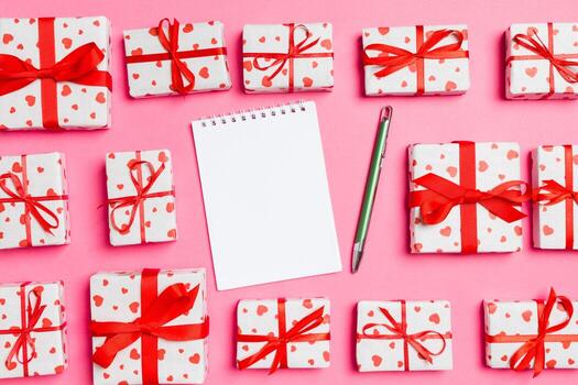 Holiday composition of notebook and gift boxes with red hearts on colorful background with empty space for your design. Top view of Valentine's Day concept photo