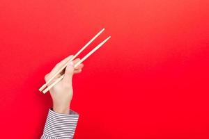 Male hand with chopsticks on red background. Traditional asian food with emty space for your design photo