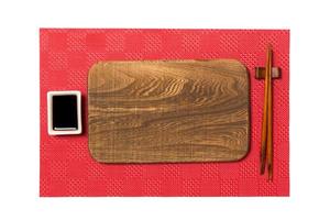 Empty rectangular brown wooden plate with chopsticks for sushi and soy sauce on red mat sushi background. Top view with copy space for you design photo