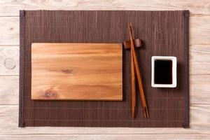 Empty rectangular wooden plate with chopsticks for sushi and soy sauce on wood background. Top view with copy space photo