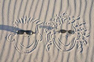 Face drawn in the sand on the beach, with sunglasses. Sand with wave pattern photo