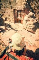 Caucasian tourist traveler sitting on viewpoint in Petra ancient city looking at the Treasury or Al-khazneh, famous travel destination of Jordan. UNESCO World Heritage site photo