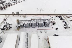 agro silos granary elevator in winter day in snowy field. Silos on agro-processing manufacturing plant for processing drying cleaning and storage of agricultural products photo