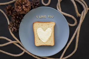 sandwich for breakfast in form of heart with cheese on a blue plate and black background with cones inscription I love you photo