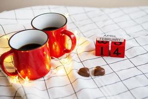 dos tazas de café en tazas rojas sobre un fondo de canfet de chocolate en forma de corazón. sorpresa de la mañana del día de san valentín. foto