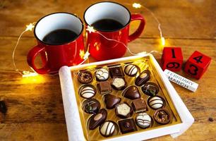 Two cups of coffee in red cups on a background of chocolate canfet. Postcard with date and month. Valentine's Day Morning Surprise. photo