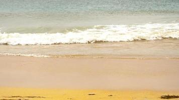 Static shot of the ocean with calm waves reaching the shore of a white sand beach on a tropical island during bright sunny day video