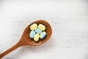 píldoras de medicina amarillas y azules en cuchara de madera sobre fondo de mesa de madera blanca en farmacia foto