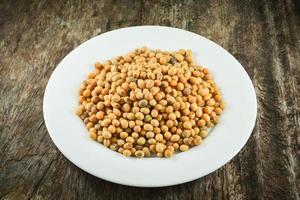 soybeans or soya beans grain seed on white plate on rustic wood background photo