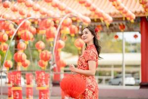 Happy Asian woman wearing traditional cheongsam qipao dress holding lantern while visiting the Chinese Buddhist temple. Chinese new year concept. Emotion Smile photo