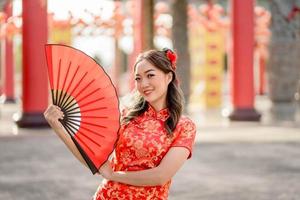 feliz festival del año nuevo chino lunar. hermosa mujer asiática con traje tradicional cheongsam qipao con ventilador en el templo budista chino. foto