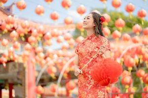 Asian woman wearing traditional cheongsam qipao dress holding lantern while visiting the Chinese Buddhist temple. Chinese new year concept photo