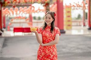 feliz Año Nuevo Chino. mujer asiática con vestido tradicional cheongsam qipao sosteniendo y mirando el antiguo dinero de oro en el templo budista chino. celebrar el año nuevo lunar chino. foto