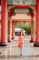 Happy Chinese new year. Asian woman wearing traditional cheongsam qipao dress holding fan while visiting the Chinese Buddhist temple photo