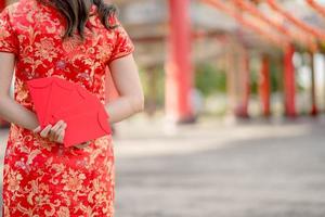 Happy Chinese new year. Beautiful asian woman wearing traditional cheongsam qipao dress and stands with her back turned holding ang pao, red envelopes in Chinese Buddhist temple. photo