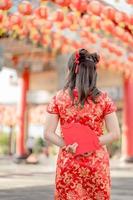 Beautiful asian woman wearing traditional cheongsam qipao dress and stands with her back turned holding ang pao, red envelopes in Chinese Buddhist temple. Celebrate Chinese lunar new year. photo