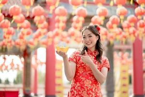 Happy Chinese new year. Asian woman wearing traditional cheongsam qipao dress holding and pointing to ancient gold money in Chinese Buddhist temple. Celebrate Chinese lunar new year. photo