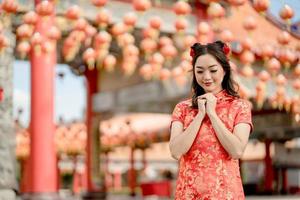 feliz Año Nuevo Chino. hermosa mujer asiática con vestido tradicional cheongsam qipao rezando por la mejor bendición y buena suerte en el templo budista chino.