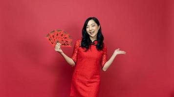 Happy woman wearing traditional cheongsam qipao dress holding blessing fortune card and hand present isolated on red background. Chinese text means great luck great profit photo