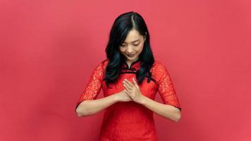 Young woman wearing traditional cheongsam qipao dress with gesture of congratulation isolated on red background. Chainese new year concept. photo