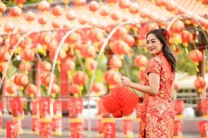 Happy Asian woman wearing traditional cheongsam qipao dress holding lantern while visiting the Chinese Buddhist temple. Celebrate Chinese lunar new year, festive season holiday. Emotion Smile photo