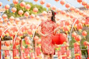 Young lady woman wearing traditional cheongsam qipao costume holding lantern in Chinese Buddhist temple. Celebrate Chinese lunar new year, festive season holiday. Emotion smile photo