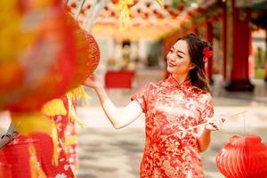 Happy Chinese new year. Asian woman wearing traditional cheongsam qipao dress looking confident holding and playing lantern while visiting the Chinese Buddhist temple photo
