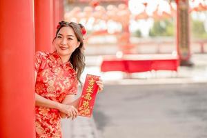 feliz Año Nuevo Chino. mujer asiática con vestido tradicional cheongsam qipao con tarjeta de bendición de la fortuna en el templo budista chino. texto chino significa bendecido por una estrella de la suerte foto