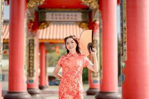 Happy Chinese new year. Beautiful asian woman wearing traditional cheongsam qipao dress holding fan while visiting the Chinese Buddhist temple. Emotion Smile photo