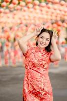 Vertical picture. Happy Chinese new year. Asian woman wearing traditional cheongsam qipao dress posing rabbit in Chinese Buddhist temple. Celebrate Chinese lunar new year, festive season holiday. photo