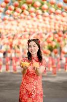 Happy Chinese new year. A young lady wearing traditional cheongsam qipao dress holding ancient gold money and orange fresh in Chinese Buddhist temple. Celebrate Chinese lunar new year. photo