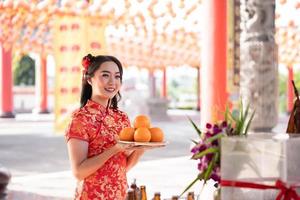 Happy Chinese new year. Beautiful asian woman wearing traditional cheongsam qipao dress holding fresh oranges in Chinese Buddhist temple. photo