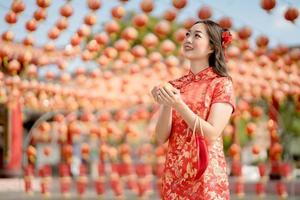 feliz Año Nuevo Chino. hermosa mujer asiática con vestido tradicional cheongsam qipao con dinero de oro antiguo y bolsa en el templo budista chino. celebrar el año nuevo lunar chino foto