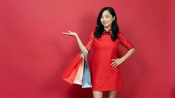 Beautiful woman wearing traditional cheongsam qipao dress holding shopping bag and present for advertise isolated on red background. Happy lunar new year photo