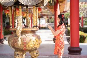 mujer asiática con vestido tradicional cheongsam qipao rezando con varitas de incienso durante el año nuevo chino o lunar, año nuevo chino